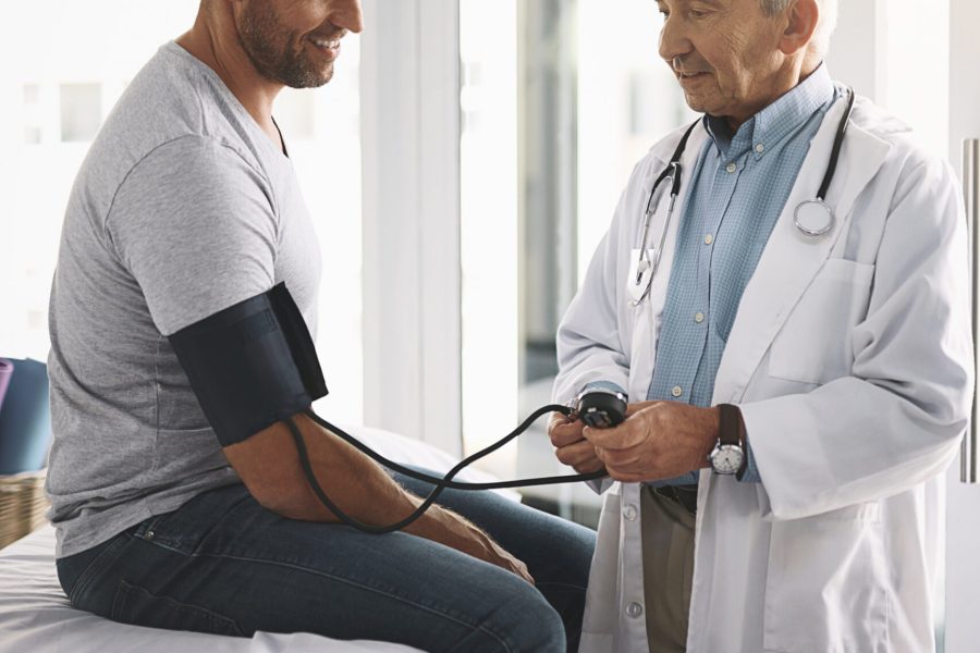 Healthcare, man and doctor in consultation for blood pressure test, checkup and assessment in clinic. Advice, patient and medical professional in office for hypertension, diabetes or health insurance.