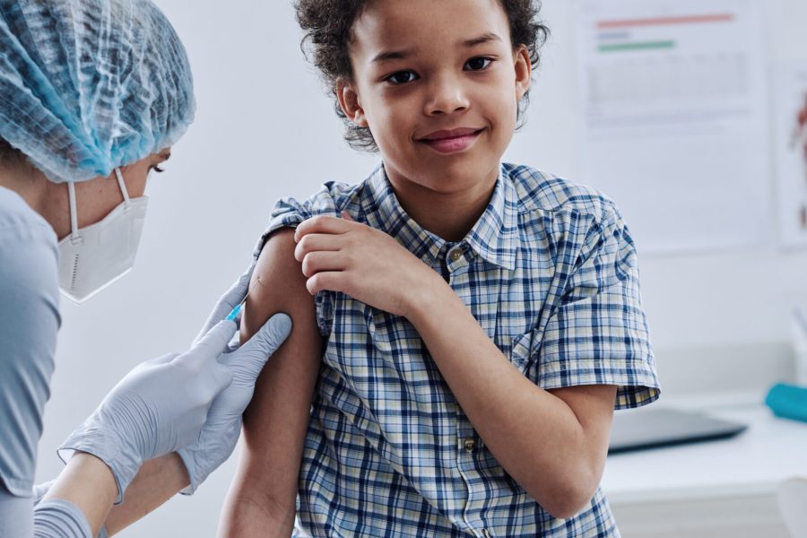 Portrait of African little boy smiling at camera while nurse giving injection in his arm at procedure room