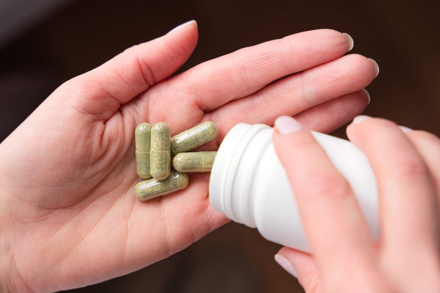Women's hand pouring herbal pills from a bottle in her hand. Vitamins, bio supplement. Close-up. Selective focus.